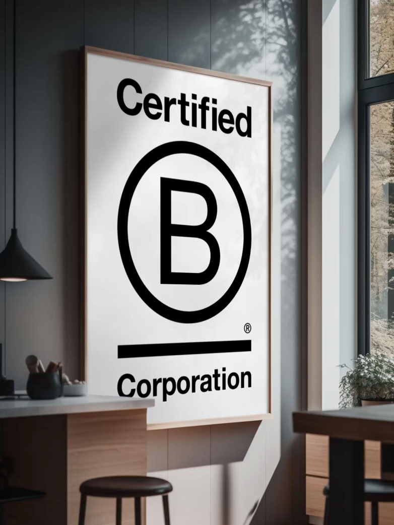 Poster met de tekst "Certified B Corporation" in een moderne kantoorruimte met een raam en een hanglamp.