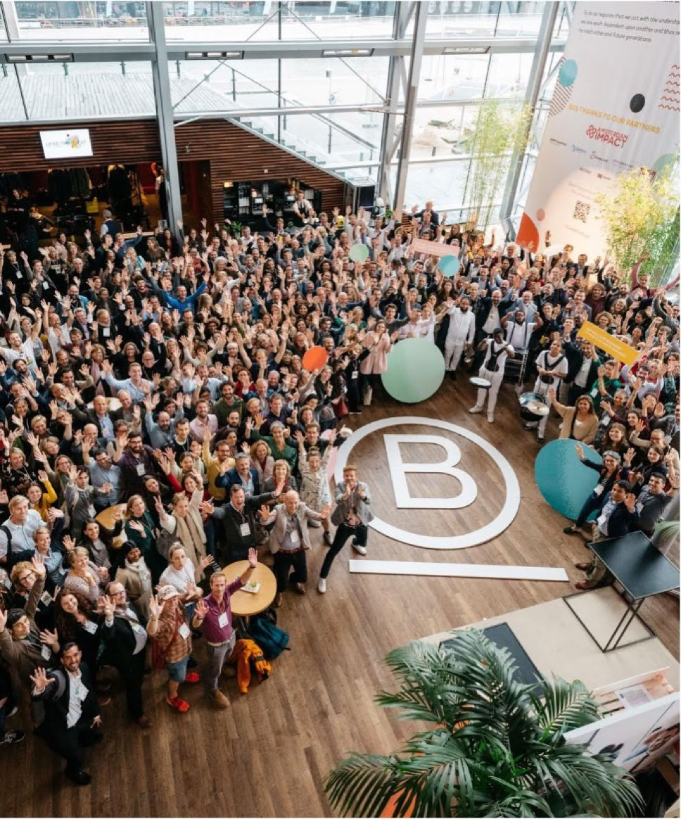 Grote groep mensen verzameld in een ruime, lichte hal met een groot "B"-symbool op de vloer.